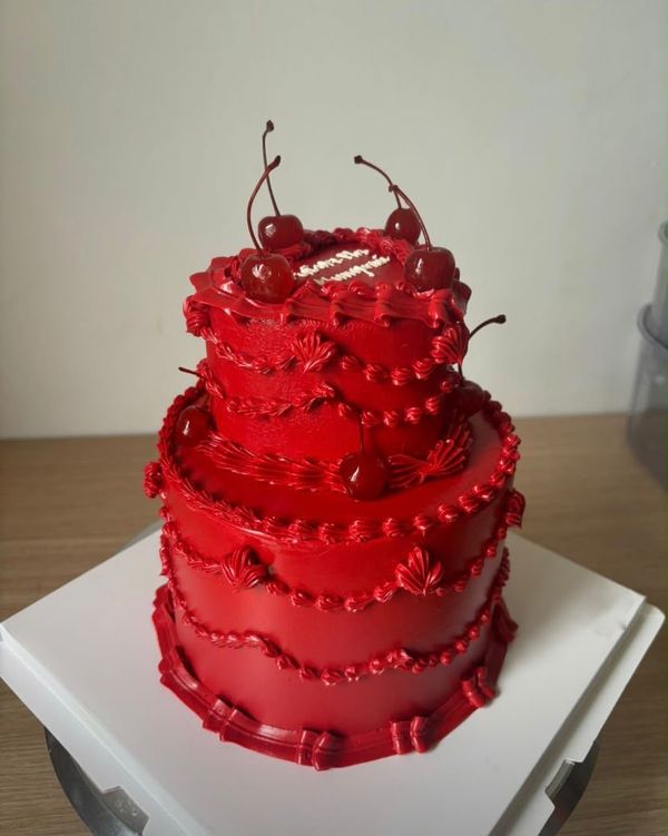 A two tier red cake with cherries and piped frills, by our baker